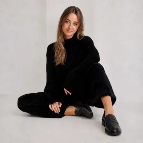 Junge Frau sitzt in schwarzem Outfit und trägt schwarze Damen Penny Loafer aus Leder