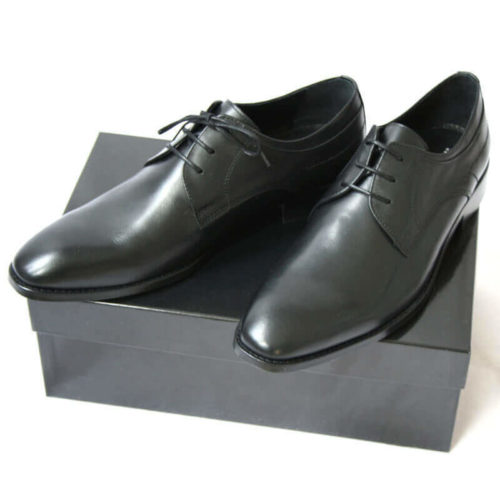 Foto von zwei schwarzen Derby Glattleder Herrenschuhen auf schwarzem Schuhkarton. Modell Stil Statement