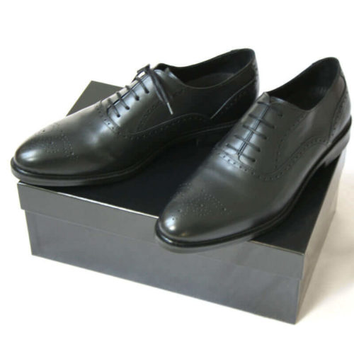 Foto von zwei schwarzen Oxford Glattleder Herrenschuhen mit Verzierung auf schwarzem Schuhkarton. Modell Oxford Plus