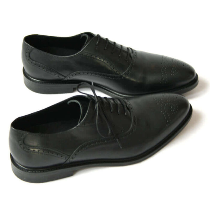 Foto von zwei schwarzen Oxford Glattleder Herrenschuhen mit Verzierung. Beide nach rechts zeigend. Einer quer stehend. Die Schuhspitzen berühren sich. Modell Oxford Plus