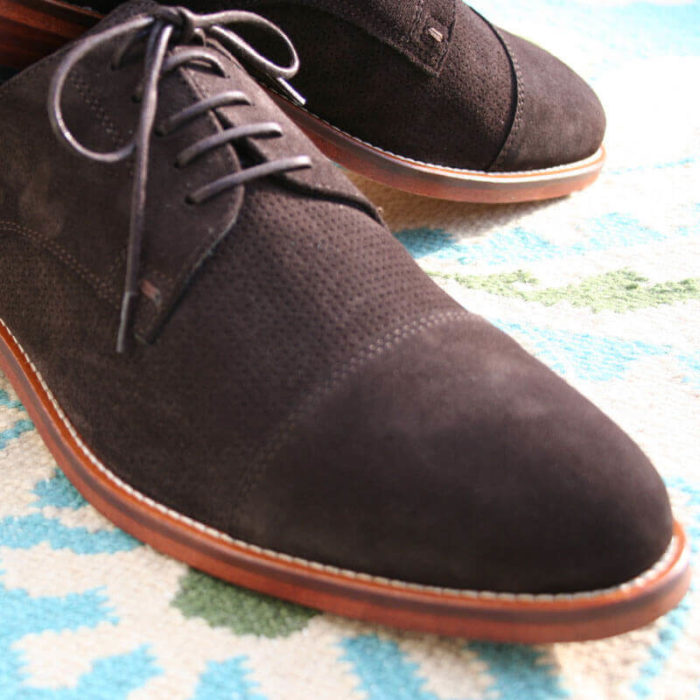 Foto von zwei mokkafarbenen Derby Rauleder Herrenschuhen mit Zehenkappe. Nahaufnahme, so dass nur der vordere Teil der Schuhe zu sehen ist. Auf Teppich. Modell Top Wildleder