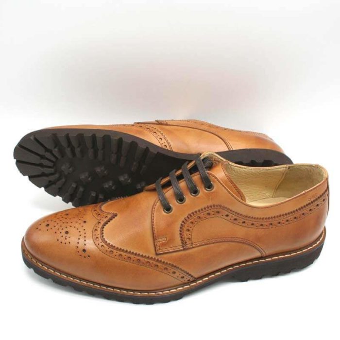 Budapester Cognac elegant, solide Herrenschuhe. Ein Schuh liegend, so dass die Gummiprofilsohle sichtbar ist, der andere stehend, nach links zeigend. Modell 372