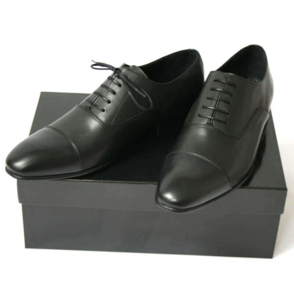 Foto von zwei schwarzen Glattleder Oxford Herrenschuhen auf schwarzem Schuhkarton. Modell Erste Wahl