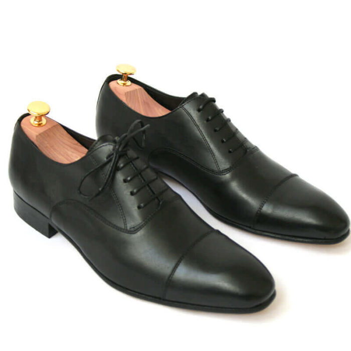 Foto von zwei schwarzen Glattleder Oxford Herrenschuhen nach schräg unten rechts zeigend mit Goldkopf-Schuhspannern. Modell Erste Wahl