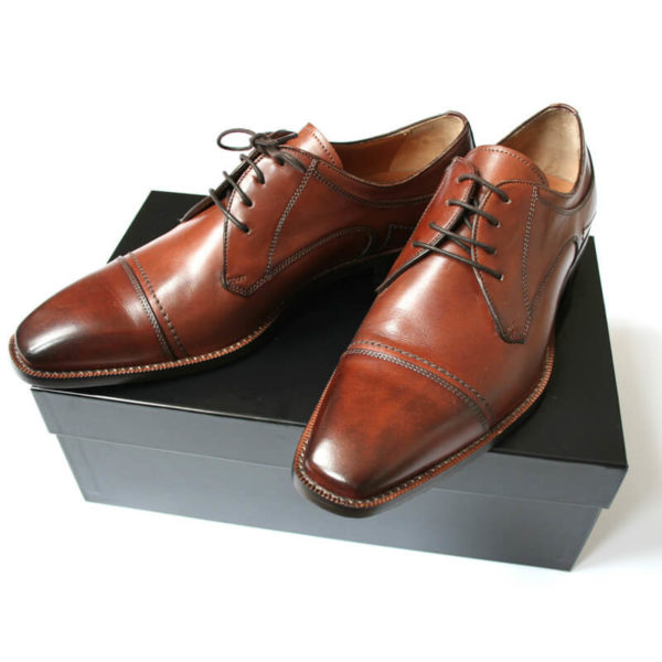 Foto Individuell und maskulin Herrenschuh Business Derby in Cognac. 2 Schuhe auf schwarzem Schuhkarton.