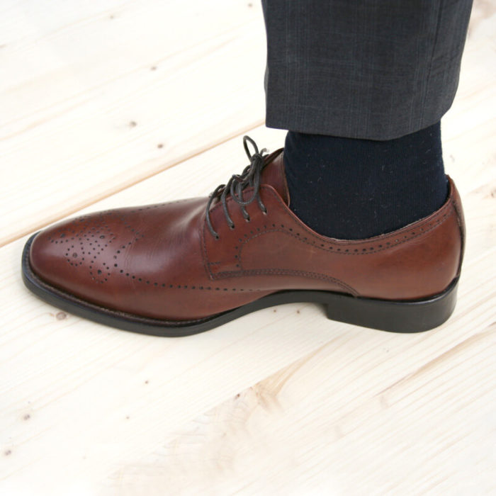 Foto-Nussbraune Business Herrenschuhe_Ein Schuh mit hochgezogenem Hosenbein nach links weisend