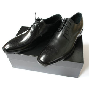 Foto zeigt das Produkt Maskuliner Klassiker Herren-Businessschuh in Schwarz mit eleganter Verzierung auf schwarzem Schuhkarton