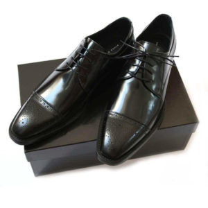 Foto-Herren Business Schuhe-Halfbrogue. 2 schwarze Schuhe auf schwarzem Schuhkarton. Modell Stattliche Eleganz